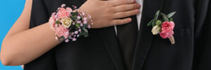 Young woman with corsage hugging her prom date on blue background, closeup
