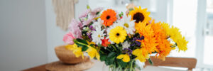 Kitchen counter table with focus on vase with huge multicolor various flower bouquet with blurred background of modern cozy white kitchen.