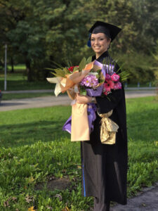A beautiful Latina graduate, holding a bouquet in her hands, smiles with pride and joy after receiving her diploma at her graduation ceremony